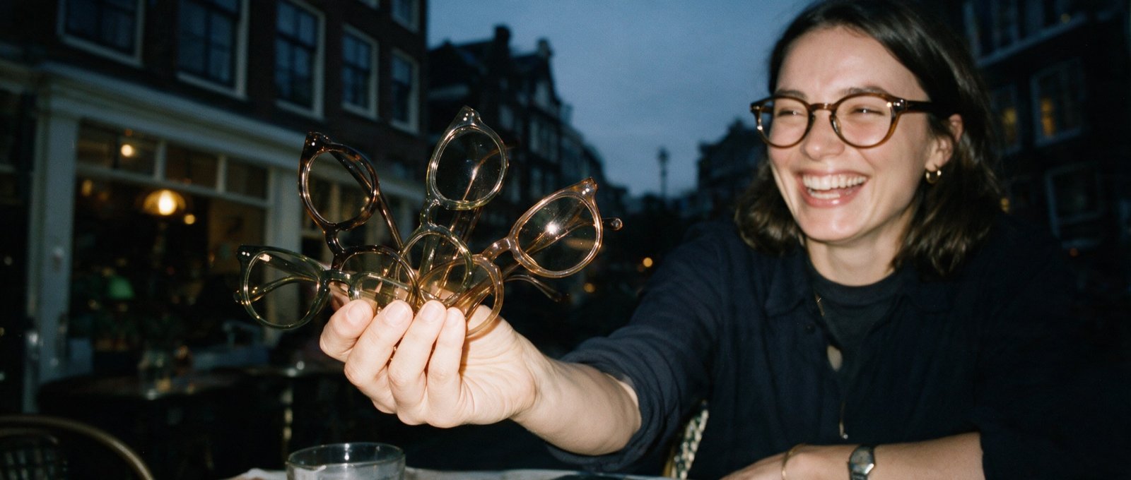 Woman on an Amsterdam terrace at dusk holding up three Bohemian frames in different colours